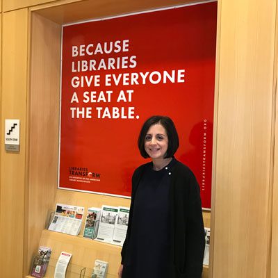 Julie in front of the Because libraries give everyone a seat at the table sign