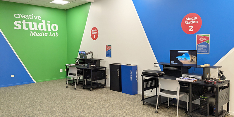 Two desks with digital equipment sitting alongside a wall with Creative Studio Media Lab displayed on it