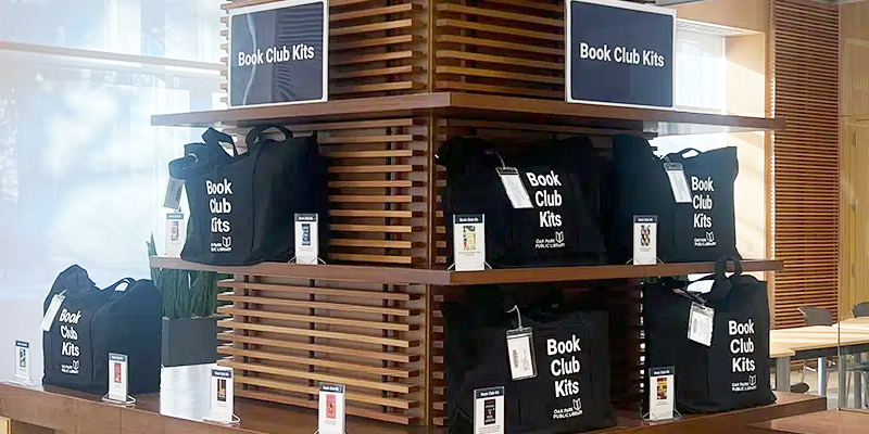 Shelf with black tote bags labeled Book Club Kit