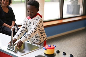 Preschooler smiling while pretending to wash hands in a play sink