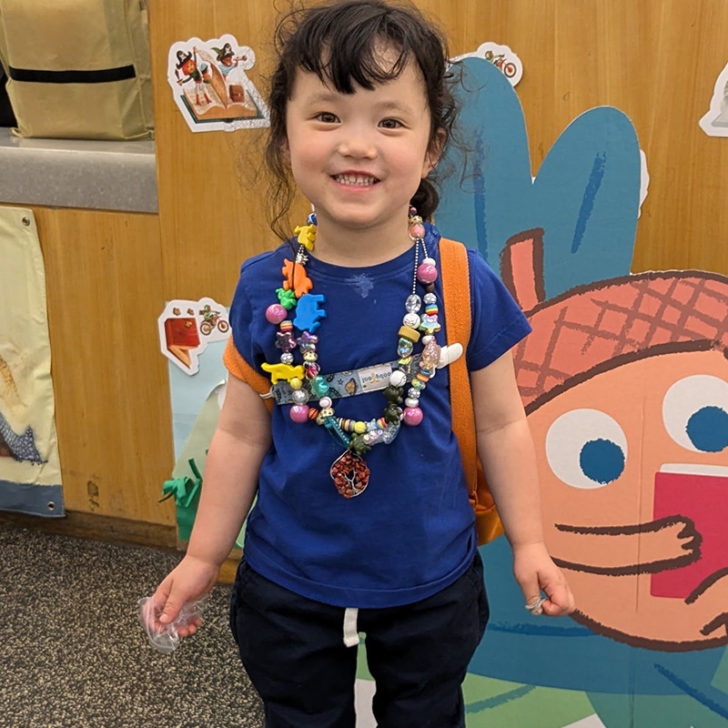 Child smiles and wears two necklaces with lots of colorful beads