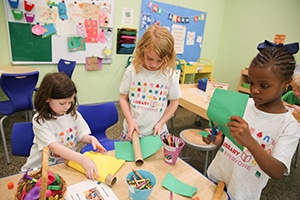 Three children using empty cardboard tubes and construction paper to craft