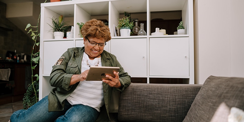 Older adult sitting on a couch smiling and looking at a tablet