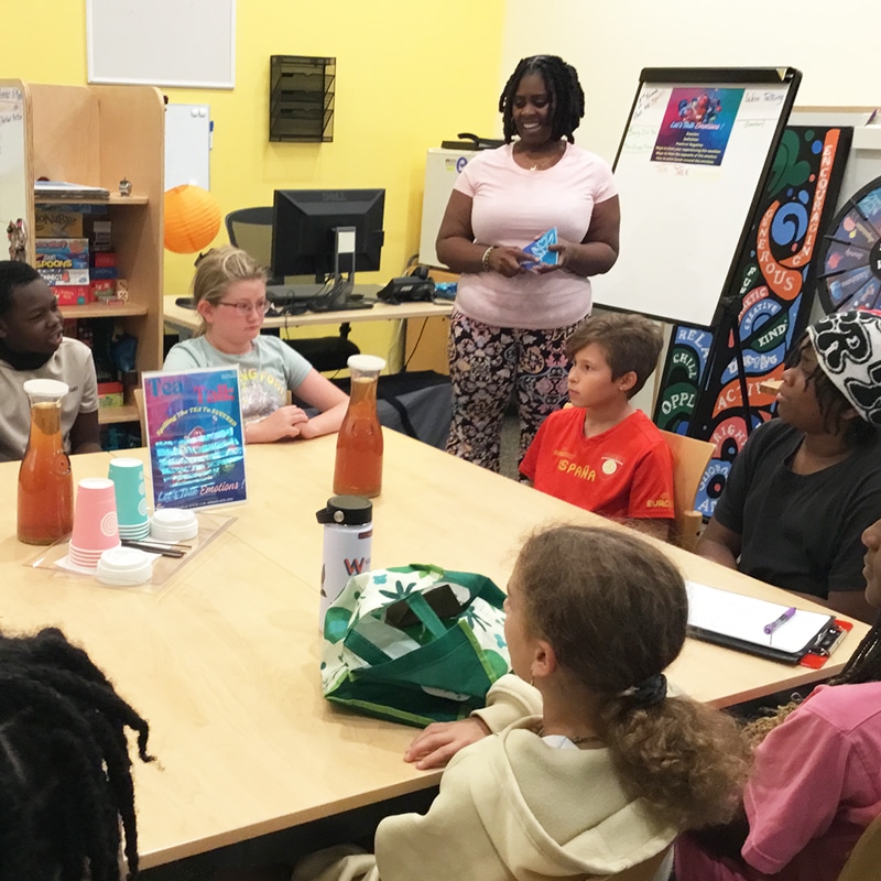 Adult stands in room with middle schoolers around a table