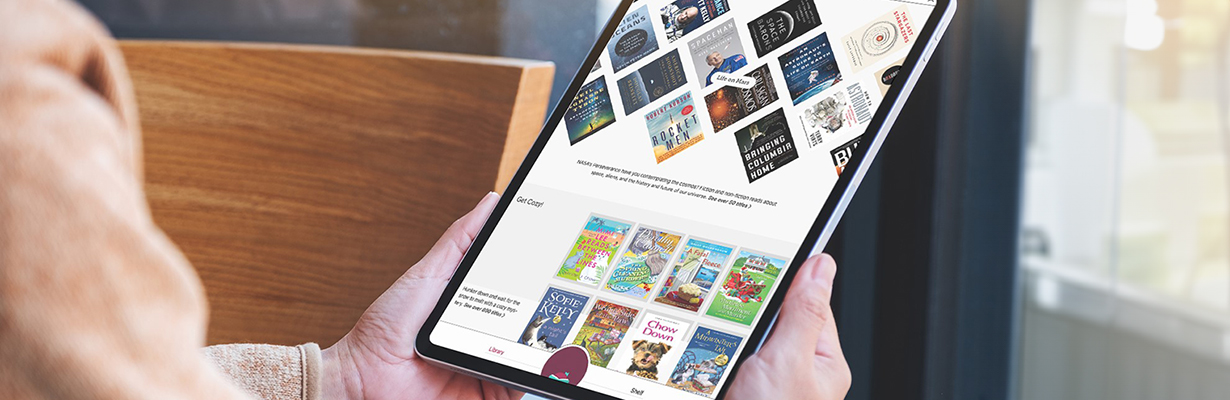 Libby app displaying book covers shown on a tablet being held by two hands